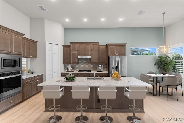 kitchen featuring a kitchen island with sink, sink, stainless steel appliances, and hanging light fixtures