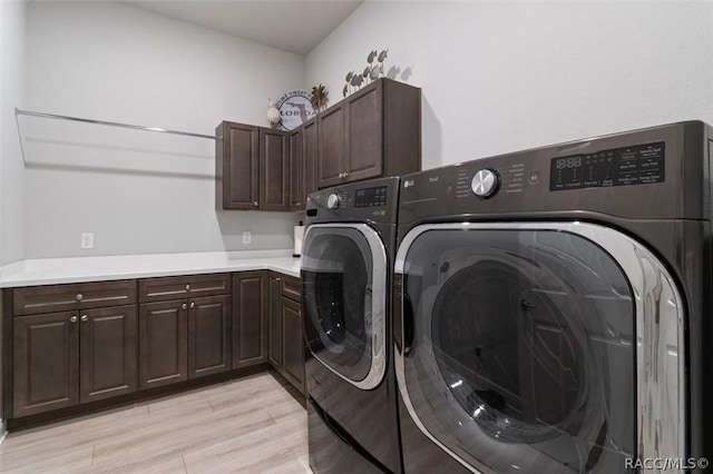 clothes washing area with cabinets, light hardwood / wood-style floors, and washing machine and clothes dryer