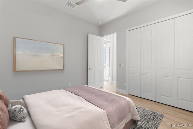 bedroom with a ceiling fan, wood finished floors, visible vents, baseboards, and a closet