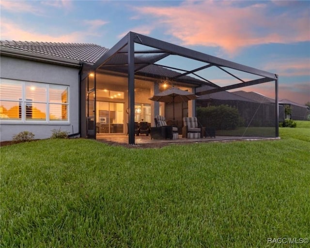 back house at dusk featuring a yard, a lanai, and a patio area