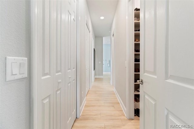 hallway with light wood finished floors, recessed lighting, baseboards, and a textured wall