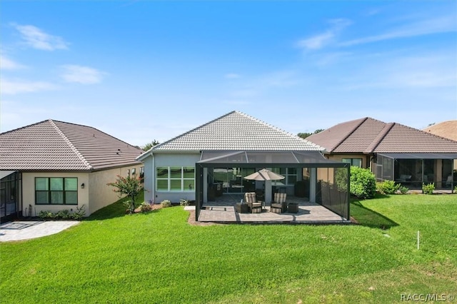 rear view of house with a lawn, glass enclosure, a tiled roof, a patio area, and stucco siding