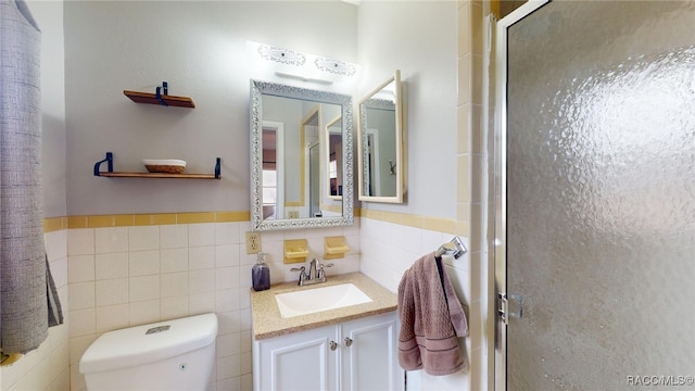 bathroom with vanity, toilet, a shower with shower door, and tile walls