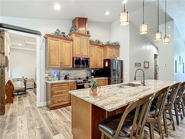 kitchen with sink, a breakfast bar area, light hardwood / wood-style flooring, decorative light fixtures, and stainless steel appliances