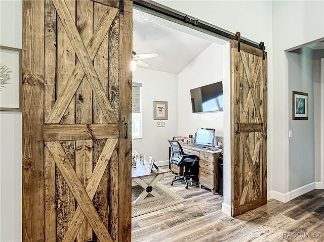 home office featuring a barn door, ceiling fan, lofted ceiling, and hardwood / wood-style flooring