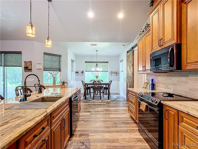 kitchen with black appliances, sink, a barn door, light stone countertops, and light wood-type flooring