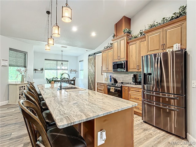 kitchen with a barn door, stainless steel appliances, a center island with sink, and lofted ceiling