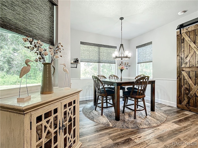 dining room with a barn door, dark hardwood / wood-style flooring, a chandelier, a textured ceiling, and wooden walls