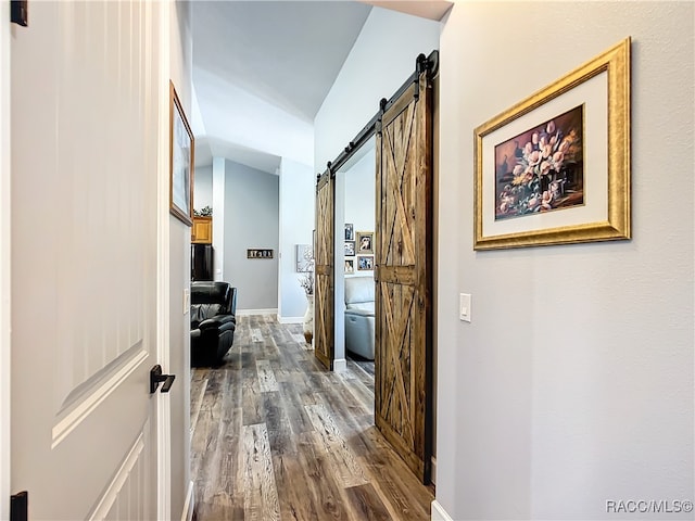 corridor featuring a barn door, dark hardwood / wood-style flooring, and vaulted ceiling