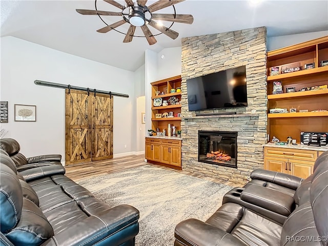 living room with vaulted ceiling, ceiling fan, a barn door, a fireplace, and light hardwood / wood-style floors