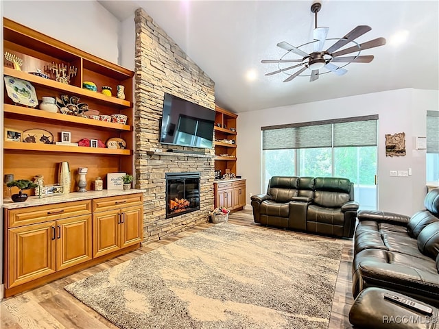 living room featuring light wood-type flooring, vaulted ceiling, ceiling fan, and a stone fireplace