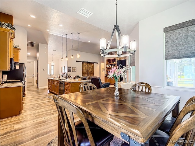 dining space featuring sink, an inviting chandelier, a barn door, a textured ceiling, and light wood-type flooring