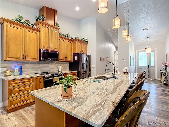 kitchen with appliances with stainless steel finishes, light wood-type flooring, a breakfast bar, a large island with sink, and decorative light fixtures