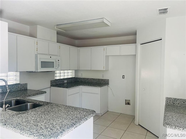 kitchen with white cabinets, stone countertops, light tile patterned flooring, and sink