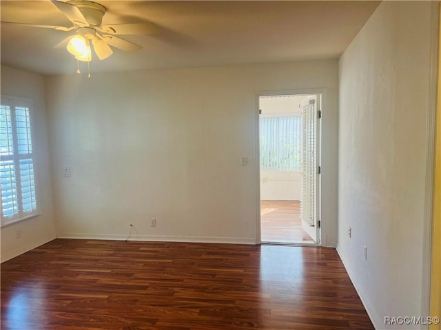 empty room featuring ceiling fan, a wealth of natural light, and dark wood-type flooring