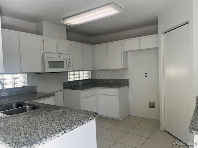 kitchen with sink, kitchen peninsula, light tile patterned flooring, and white cabinetry