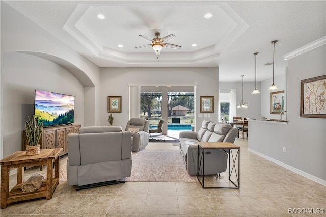 living area featuring light tile patterned floors, recessed lighting, ceiling fan with notable chandelier, baseboards, and a tray ceiling