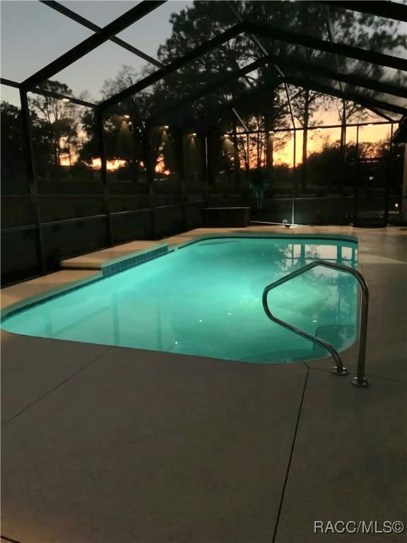 pool at dusk featuring glass enclosure, an outdoor pool, and a patio