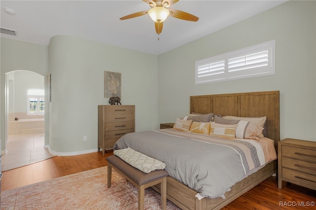 bedroom with arched walkways, visible vents, ensuite bath, and wood finished floors