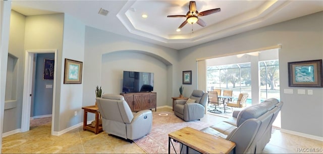 living area with a tray ceiling, visible vents, ceiling fan, and baseboards