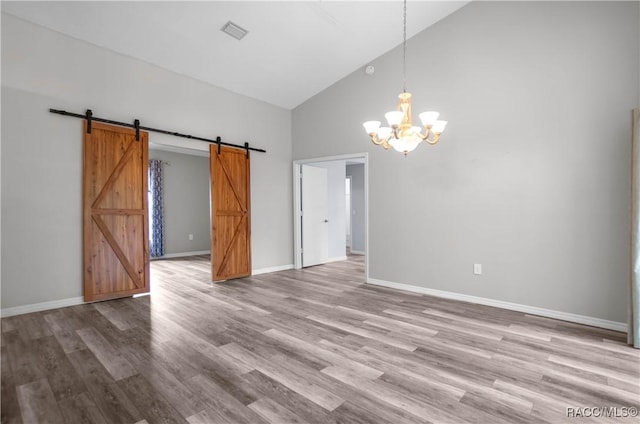 empty room featuring light wood finished floors, a chandelier, a barn door, high vaulted ceiling, and visible vents