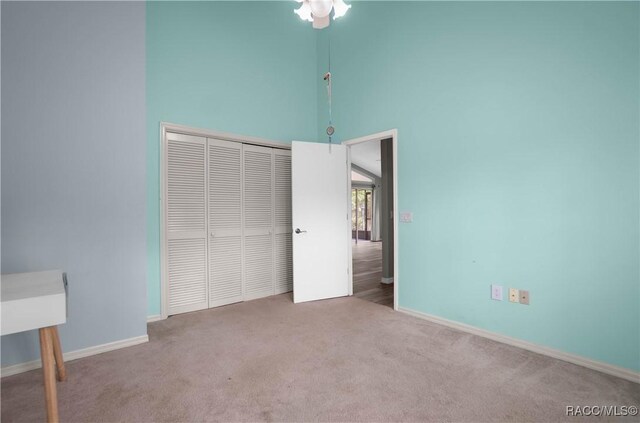 unfurnished bedroom with a closet, baseboards, a high ceiling, and carpet floors