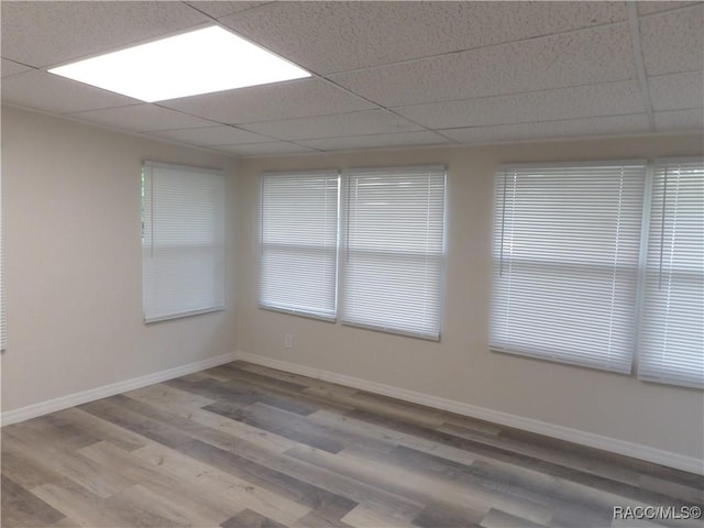 empty room with a paneled ceiling, baseboards, and wood finished floors