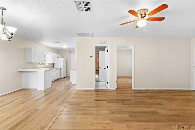 unfurnished living room with a textured ceiling, ceiling fan with notable chandelier, light hardwood / wood-style floors, and sink