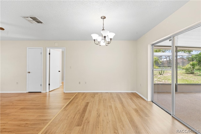 spare room with light wood-type flooring, a textured ceiling, and a chandelier