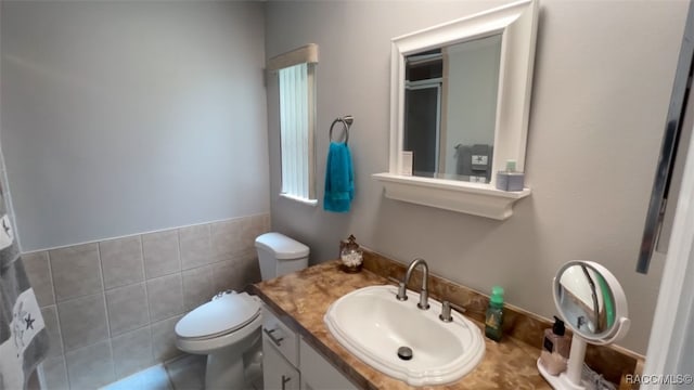 bathroom featuring tile patterned floors, vanity, toilet, and tile walls