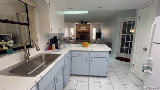 kitchen featuring sink, white cabinets, kitchen peninsula, a fireplace, and light tile patterned flooring