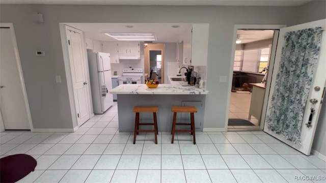 kitchen featuring white appliances, kitchen peninsula, light tile patterned floors, a kitchen bar, and white cabinetry