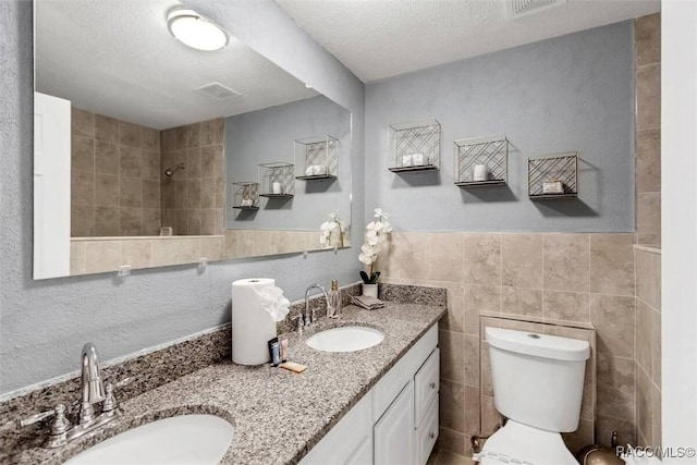1316 Lake Ariana Blvd, Auburndale, FL 33823 - bathroom featuring double vanity, tile walls, toilet, a wainscoted wall, and a textured ceiling