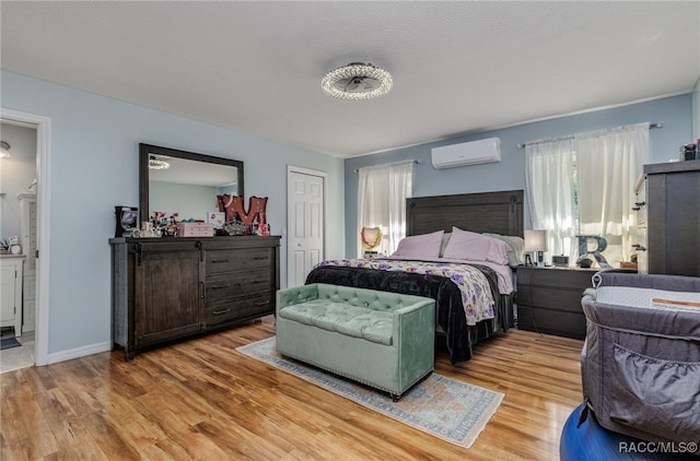 bedroom featuring an AC wall unit, ensuite bathroom, a textured ceiling, and light wood-type flooring