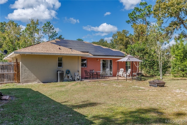 back of house with a lawn, a patio area, a fire pit, and solar panels