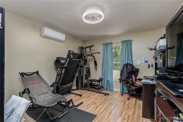 workout area with an AC wall unit, a textured ceiling, and light wood-type flooring