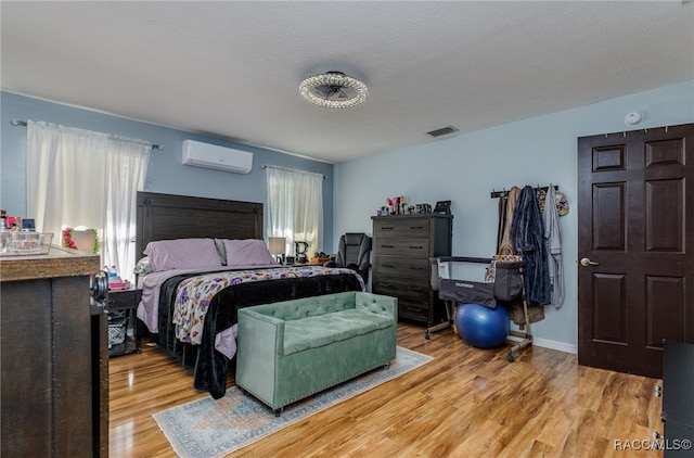 bedroom with a wall mounted air conditioner, a textured ceiling, and light hardwood / wood-style flooring