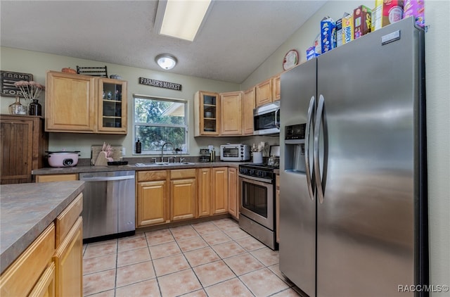 kitchen featuring light brown cabinets, sink, vaulted ceiling, light tile patterned floors, and appliances with stainless steel finishes