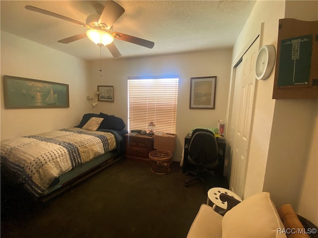 bedroom with a textured ceiling, a closet, dark carpet, and ceiling fan