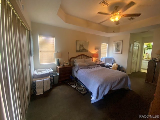 bedroom featuring a raised ceiling, multiple windows, ceiling fan, and dark colored carpet