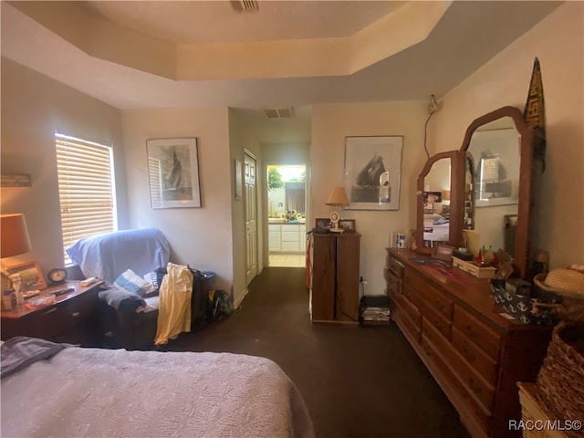 carpeted bedroom with a raised ceiling and connected bathroom