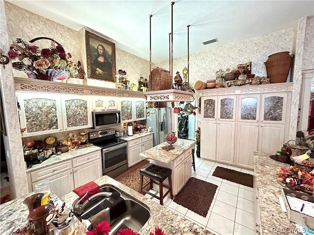 kitchen featuring a center island, sink, light stone countertops, light tile patterned floors, and stainless steel appliances