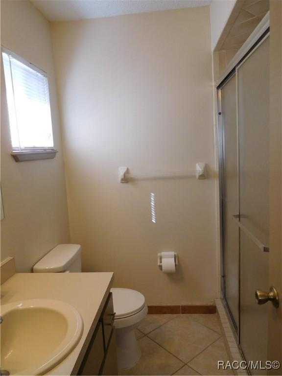 bathroom with vanity, tile patterned floors, a shower with door, and toilet