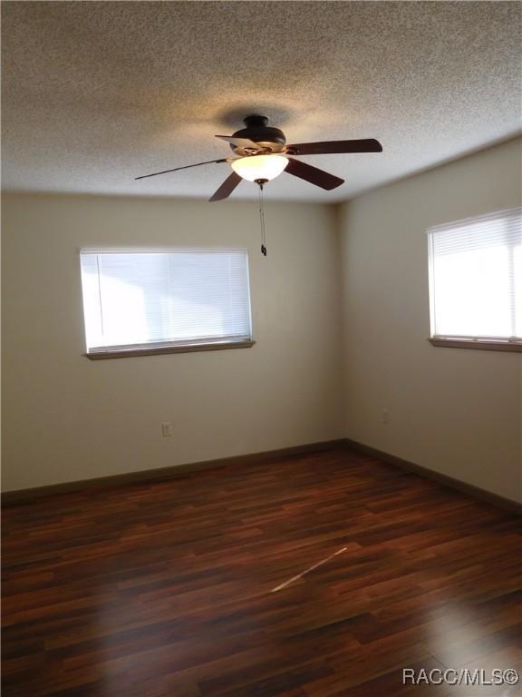 empty room featuring a textured ceiling, plenty of natural light, dark hardwood / wood-style floors, and ceiling fan