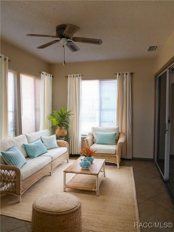 tiled living room with ceiling fan, plenty of natural light, and a textured ceiling