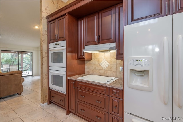 kitchen featuring tasteful backsplash, white appliances, light stone countertops, and light tile patterned floors