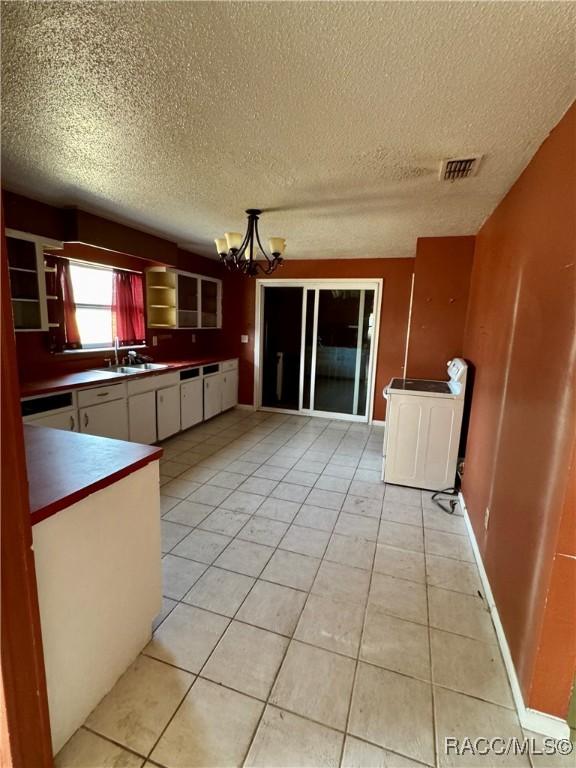 kitchen with white cabinetry, sink, a notable chandelier, washer / clothes dryer, and light tile patterned floors