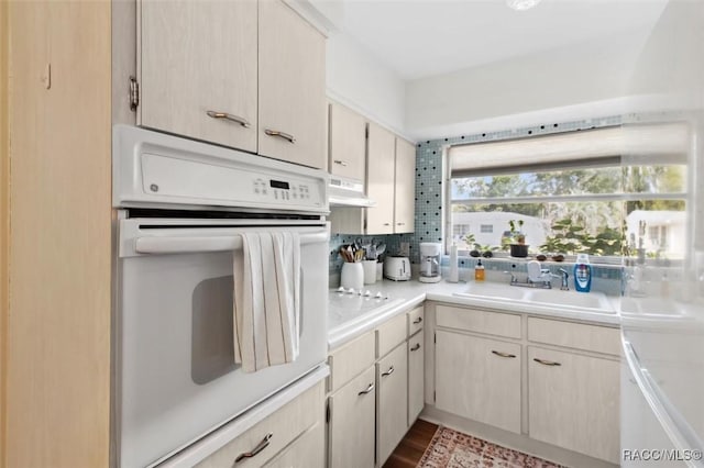 kitchen featuring light countertops, white oven, a sink, and under cabinet range hood