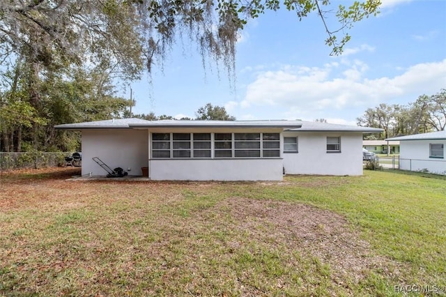 rear view of house with a lawn, fence, a sunroom, and stucco siding