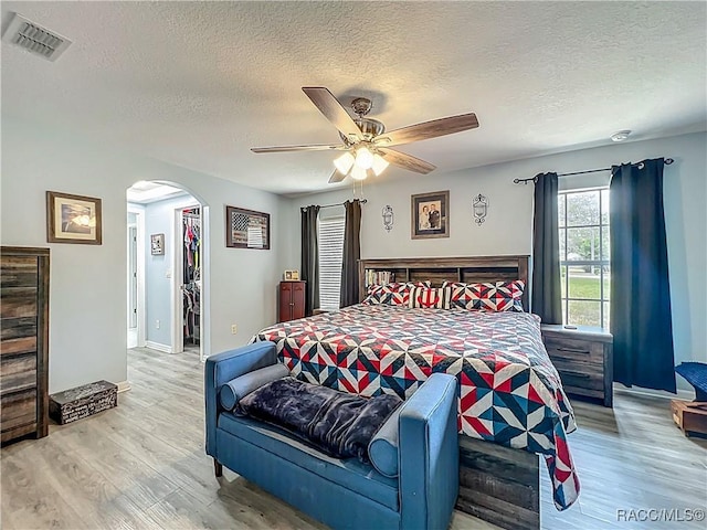 2478 W Angola Dr, Beverly Hills, FL 34465 - bedroom featuring arched walkways, a textured ceiling, wood finished floors, a spacious closet, and a ceiling fan